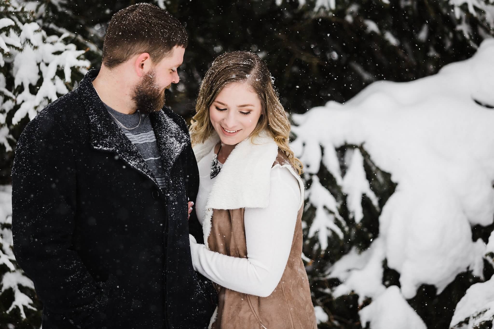 Girl looking towards the ground smiling as her fiance looks at her during their winter engagement session