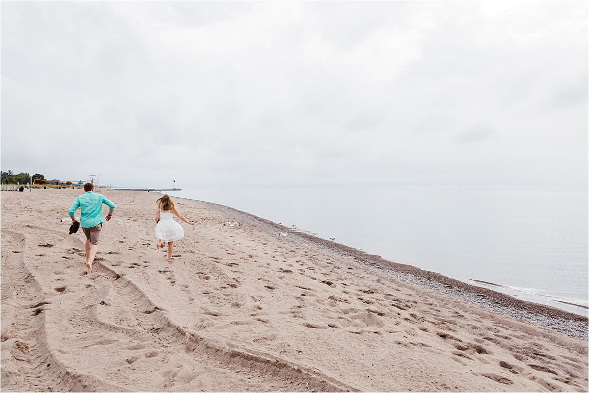 Engaged couple chasing seagulls on the beach in Grand Bend, ON during their engagement session