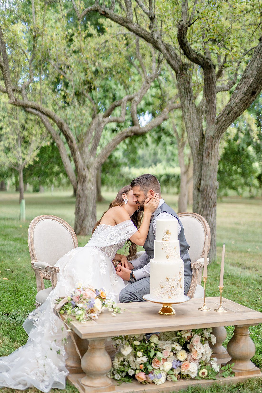 Bride and groom kissing in the orchard at sweetheart table during their Kurtz orchards
