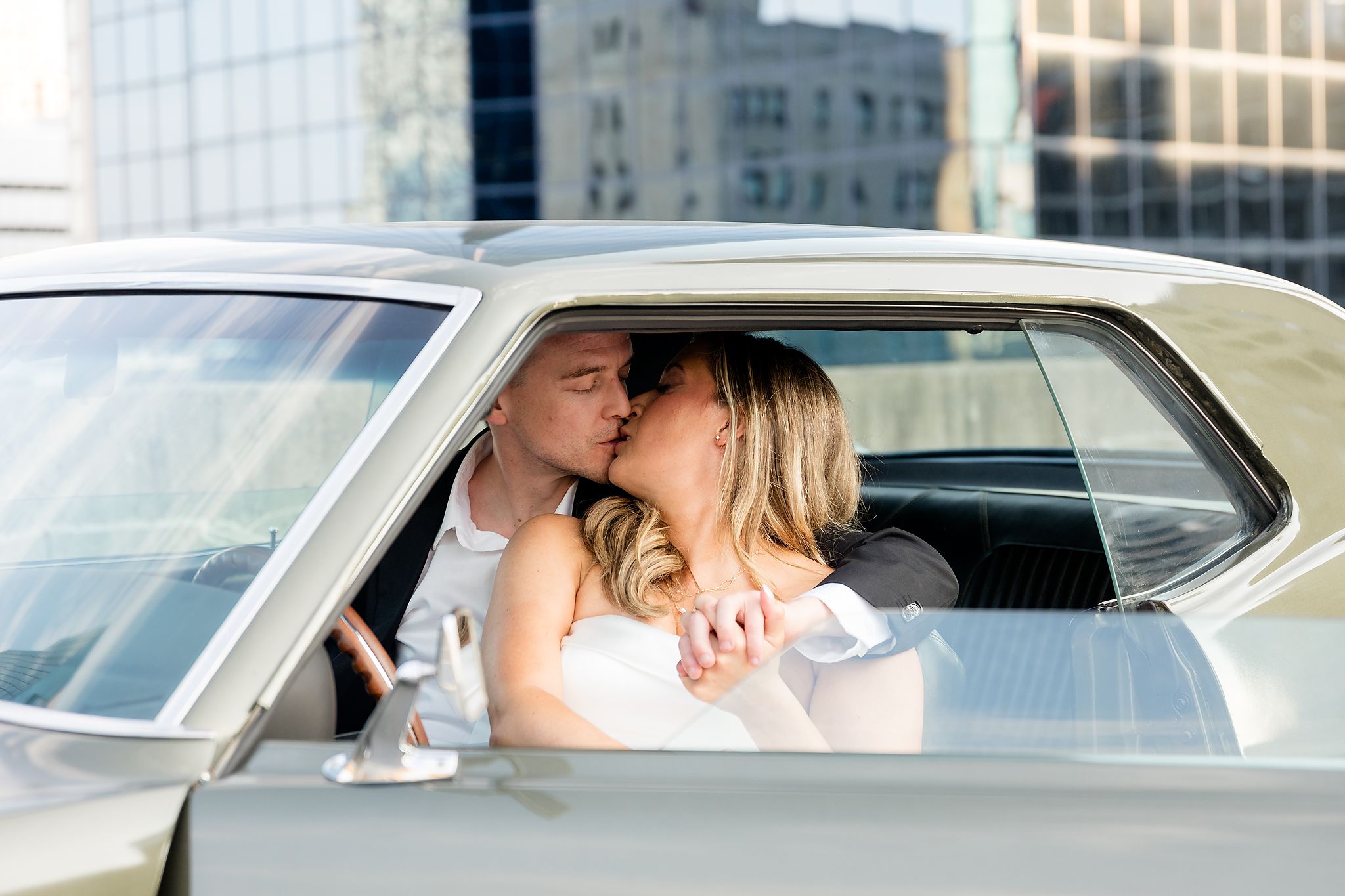 Engaged couple kissing on a rooftop in a vintage car